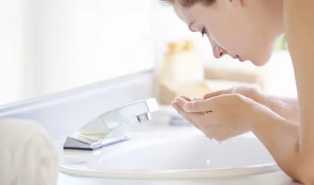 Une femme se nettoie le visage devant un mirroir avec un gel moussant